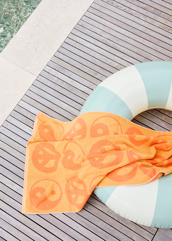 Petites Pommes Calile Pool Float close up on deck with towel. It is a striped pool ring in mint and cream for adults.