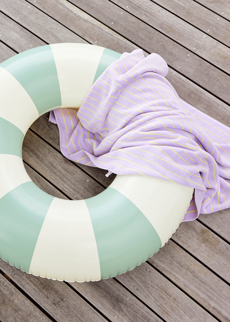 Petites Pommes Calile Pool Float close up on deck with towel. It is a striped pool ring in mint and cream for adults.