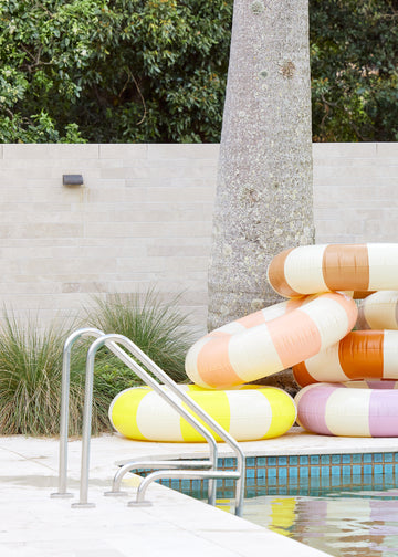 Petites Pommes Limonata pool float stacked with other striped pool floats. It is a striped pool ring in neon yellow and cream for adults.