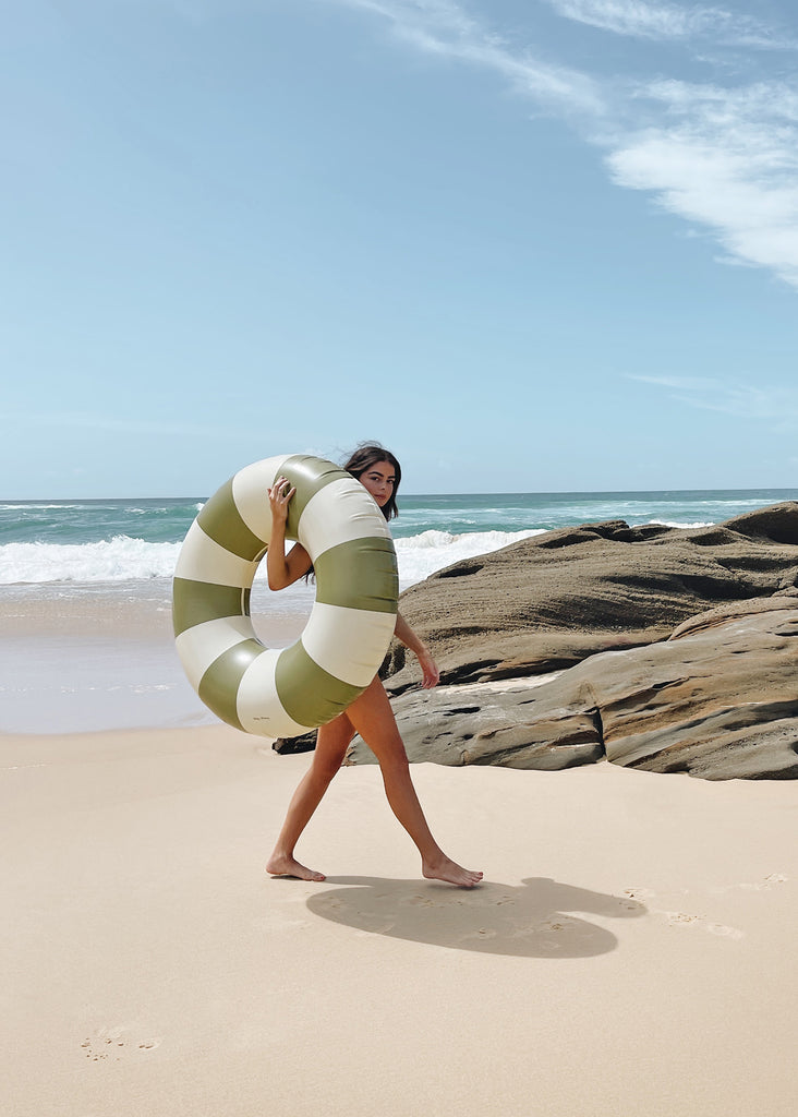 Petites Pommes Terra Verde Pool Float being held by an adult woman to show size. It is a striped pool ring in olive green and cream for adults.